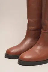 Bota de caña alta color marrón, confeccionada en cuero vacuno con forro y plantilla de cuero. Tiene suela de goma negra y un diseño de caña ancha.