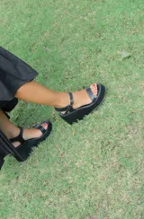 Sandalia de plataforma negra con tira ancha en el empeine y tira fina ajustable con hebilla dorada en el tobillo.