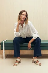 Camisa blanca de manga larga con cuello clásico y botones de nácar. Presenta detalles calados en el frente.