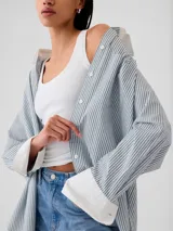Camisa de corte oversize con estampado de rayas verticales finas en tonos rosados sobre fondo claro. Presenta cuello clásico, cierre frontal con botones, bolsillo en el pecho y puños anchos con botones.