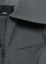 Chaqueta entallada de color gris con diseño de rayas verticales finas. Presenta cuello camisero, cierre frontal de cremallera doble y bolsillo de ribete en el pecho.
