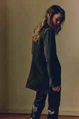 Vestido corto de corte holgado en tejido con textura levemente arrugada. Presenta cuello elevado, pliegues en un hombro que crean un efecto drapeado frontal, mangas largas con puños rectos y cierre oculto en la espalda.