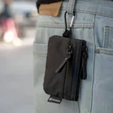 Billetera tipo pouch color negro, fabricada en material impermeable xPac X21. Cuenta con cierre principal, bolsillo frontal con cierre y tiradores ergonómicos. Incluye tecnología de bloqueo RFID.