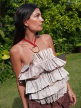 Collar tipo choker de cinta roja con un dije metálico grande en forma de 'D' hueca de color dorado.