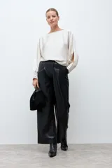 Blusa de satén color crudo, con cuello bote, mangas largas con aberturas laterales y puños abotonados.