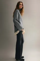 Buzo de punto holgado con mezcla de lana y mohair, color gris. Presenta cuello alto, hombros caídos y mangas largas. El bajo está decorado con un ribete de encaje en color crema en contraste.