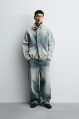 Cazadora relaxed fit de denim de algodón con efecto lavado degradado de azul a blanco. Tiene cuello subido, manga larga, bolsillos laterales en la costura de la cadera y acabados con elástico interior. El cierre frontal es con cremallera oculta por una solapa con botones a presión.