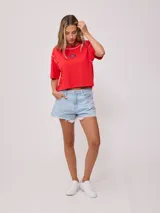 Remera blanca de algodón con corte cropped y calce holgado. Tiene cuello redondo con ribete azul y logo de la marca estampado en el pecho.