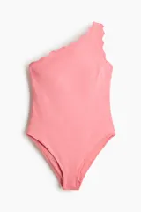 Malla enteriza de un hombro color rosado, con ribetes festoneados en el escote asimétrico y bretel, y piernas de corte alto.