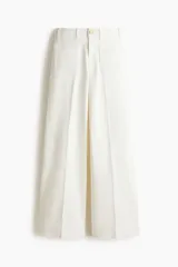 Jean de denim de algodón blanco con leve elasticidad, tiro alto y diseño de pierna ancha (wide leg). Cuenta con bolsillos de parche delanteros, botón metálico con diseño y pliegues marcados al frente y en la espalda.