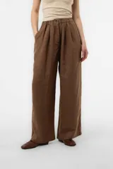 Pantalón de lino marrón de calce relajado y pierna amplia, con cintura elastizada en la parte posterior, botón delantero, bolsillos laterales y pinzas frontales.