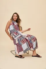 Vestido largo de silueta amplia y caída fluida, con escote halter fruncido y falda con recorte. Presenta diseño geométrico multicolor a rayas en tonos bordó, azul, celeste y beige.