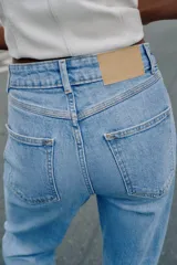 Jeans de tiro alto con diseño mom fit, tobilleros, de cinco bolsillos y cierre frontal con cremallera y botón, en color azul claro con efecto deslavado.