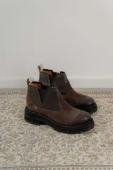 Bota tipo chelsea de punta redonda, confeccionada en una combinación de cuero texturizado y gamuza en tonos marrones. Presenta elásticos laterales negros y una suela track robusta de goma negra.