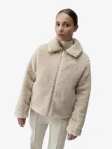Chaqueta reversible de diseño urbano, confeccionada en tejido polar estilo sherpa color beige con cierre frontal completo y cuello camisero. Cuenta con aislamiento térmico y relleno vegano, ideal para bajas temperaturas.