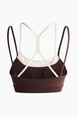 Top deportivo en tejido funcional de color marrón con tirantes dobles en color crudo y diseño de superposición. Cuenta con escote redondo y copas con relleno extraíble.