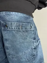 Pantalón jeans baggy de corte amplio y relajado, color azul con efecto deslavado y detalles de costuras horizontales deshilachadas.