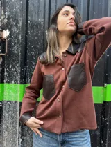Camisa de tejido de punto color marrón con cuello, bolsillos frontales, puños y hombros de cuero sintético en color marrón oscuro, y cierre frontal con botones.
