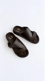 Sandalias de cuero color marrón con diseño asimétrico de tiras y plantilla anatómica. Tienen ajuste lateral con velcro y suela plana.