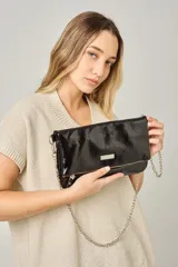Sobre de mano tipo clutch en color negro con acabado charol brillante. Cuenta con una cadena metálica plateada extraíble para usar al hombro, cierre principal y placa metálica decorativa con logo en la parte frontal.