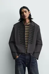 Chaqueta cropped de algodón con cuello mao y manga larga. Presenta un diseño de inspiración militar con alamares decorativos en contraste en el frente, trabillas en los hombros y cierre frontal con ganchos metálicos.