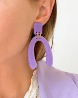 Aros colgantes de acrílico color lila, con forma geométrica rectangular en la parte superior y forma de U en la parte inferior.