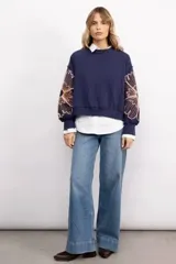 Buzo negro de cuello redondo con diseño de flores bordadas en las mangas. Presenta un corte holgado y puños elásticos.