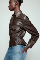Cazadora de efecto piel con cuello solapa, manga larga y cierre frontal con botones. Presenta falsos bolsillos con solapa en el delantero y bajo con acabado peplum.