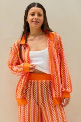 Conjunto de dos piezas tejido a crochet con diseño de ondas en tonos naranja, rosado y amarillo, compuesto por una camisa de manga larga y un pantalón largo de corte recto.