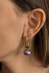 Aros tipo argolla alargada de acero dorado con dije de perla en tono violeta metalizado.