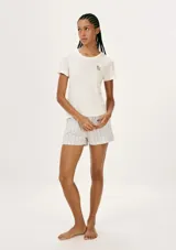 Pijama de dos piezas compuesto por una remera manga corta color blanco hueso con un pequeño bordado de flor en el pecho, y un short de tiro medio con estampado de rayas verticales finas en tonos beige y rosado.