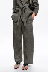 Pantalón tobillero de corte barrel color gris, confeccionado en mezcla de algodón y lino. Presenta cierre frontal con corchete oculto y cremallera, tiro medio, bolsillos delanteros en costura y bolsillos tipo plastrón en la parte trasera.