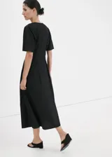 Vestido midi de corte evasé color negro, con diseño largo, cuello en pico, detalles fruncidos y manga corta. Cuenta con cierre de cremallera en la parte posterior.