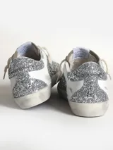 Zapatillas bajas Golden Goose modelo Super-Star, con glitter plateado, estrella de gamuza gris y detalles en cuero blanco.