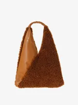 Cartera tipo hobo de silueta envolvente, con asa integrada. Presenta un diseño bicolor y bimanual: una cara es de cuero texturizado color caramelo y la otra cara es de tejido de pelo sintético (borreguito) color marrón oscuro.