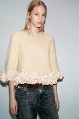 Jersey de punto color crema con cuello redondo y mangas tres cuartos. Presenta un diseño holgado con el ruedo decorado con aplicaciones de flores de tela en relieve.