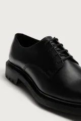 Zapato de vestir tipo derby fabricado en piel color negro, con horma redonda y suela track dentada.