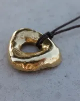 Collar con dije de forma irregular en tonos dorados y plateados, suspendido de un cordón doble de algodón negro.