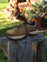 Championes de trekking color marrón, con diseño robusto y suela dentada para mayor tracción. Presenta cordones jaspeados, detalles en naranja y refuerzos laterales, ideal para actividades al aire libre.