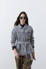 Sobrecamisa de jean color negro con silueta relajada, cuello camisero, cierre frontal con botones metálicos, bolsillos frontales y cinturón ajustable en la cintura.