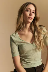 Top de manga corta confeccionado en tejido jacquard con textura en relieve. Presenta escote en V con diseño cruzado y corte al cuerpo.