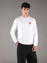 Buzo Calvin Klein blanco de manga larga, confeccionado en algodón regenerado y poliéster reprocesado con interior de felpa suave. Presenta cuello redondo, puños y dobladillo acanalados, y un estampado frontal con texto y un cuadrado rojo.