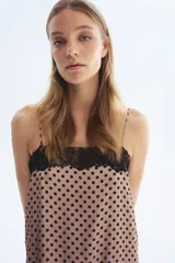 Vestido midi de satén color beige con estampado de lunares negros, breteles finos ajustables, escote recto con ribete de encaje negro, tajo lateral con detalle de encaje y bajo con terminación de encaje.