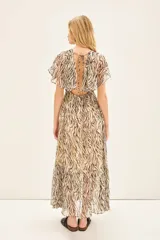 Vestido largo de viscosa jacquard con estampado de cebra en tonos marrón y negro, con detalles en lurex dorado. Presenta escote en V cruzado, elástico en la cintura y mangas cortas con volados.