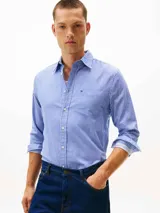 Camisa de hombre de manga larga, confeccionada en sarga de algodón mercerizado, con diseño de rayas verticales azules y blancas. Presenta cuello con botones, bolsillo de parche en el pecho con logo bordado de Tommy Hilfiger y puños redondeados con botón.