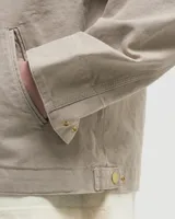 Campera Carhartt modelo Detroit color beige, con cuello camisero, cierre frontal con cremallera, bolsillos laterales y bolsillo en el pecho con logo de la marca.