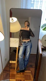 Top de encaje negro con escote bardot y mangas largas. Presenta un diseño ajustado al cuerpo con acabado delicado.