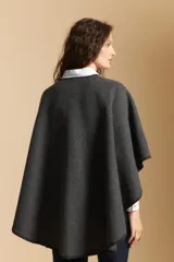 Poncho de tejido suave color beige con diseño envolvente y terminaciones con costuras decorativas en contraste color negro. Presenta un detalle de lazo frontal integrado.