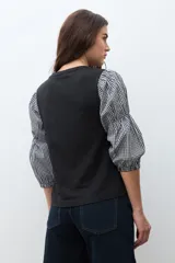 Remera de algodón negra con mangas abullonadas de tela con estampado vichy en blanco y negro, puños elásticos y cuello redondo.