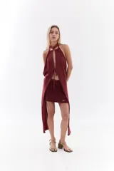 Top halter color bordó con tejido de lurex, escote con tiras cruzadas en el cuello y abertura frontal pronunciada con cordones ajustables.